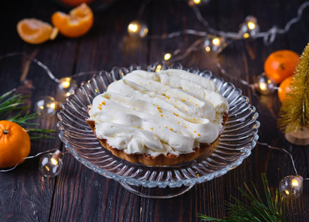 Christmas mini tart with mandarin filling and cream on glass cake stand on dark wooden background....