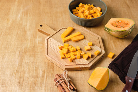 Cubed pumpkin on a wooden board and in a bowl, pumpkin pieces on the table. Cooking pumpkin dishes. Thanksgiving Day. Copyspaceの写真素材