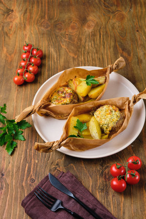 Portioned hearty dinner, baked cutlets with cheese sauce and baked country-style potatoes in a parchment boat shape. Comfort food. Dishes for a family dinner or lunchの写真素材
