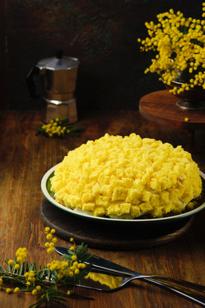 Mimosa sponge cake with custard cream sprinkled with yellow sponge cake on a green plate on a brown wooden background. Spring desserts for March 8. Italian cuisineの写真素材