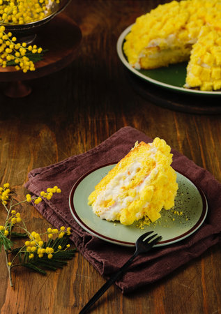 Mimosa sponge cake with custard cream sprinkled with yellow sponge cake on a green plate on a brown wooden background. Spring desserts for March 8. Italian cuisineの写真素材