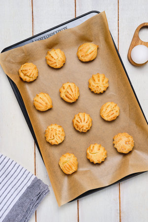 Baked choux pastry profiteroles on a baking sheet with baking paper on a white wooden background....