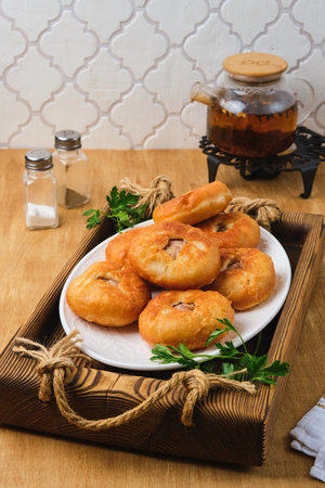 Belyashi, deep-fried round pies made of yeast dough with minced meat and onion filling on a white plate on a wooden tray. Deep-fried pastries. Tatar cuisine.の写真素材