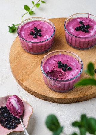 Berry dessert, yogurt mousse or jelly with blueberries in glass bowls on a wooden board on a light concrete background. No-bake desserts. Healthy foodの写真素材