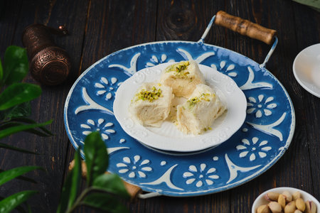 Eastern sweet, pishmaniye or cotton halva with pistachios on a white plate on a dark wooden...