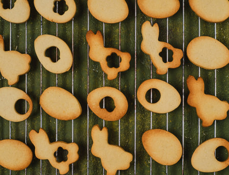 Baked Easter shortbread cookies in the shape of bunnies, eggs and flowers on a metal grid on a green concrete background before being decorated. Happy Easter. Easter treatsの写真素材