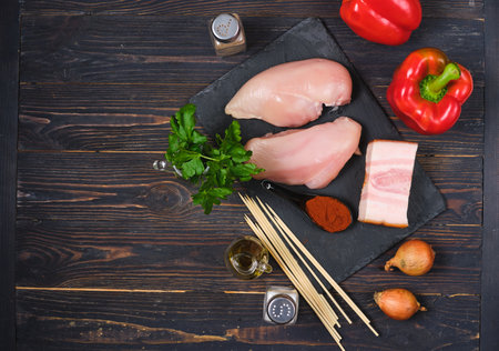 Prepared ingredients for cooking chicken with sweet pepper and onion on wooden skewers on a dark wooden background. Kebab, chicken on skewers. Grill season, barbecueの写真素材