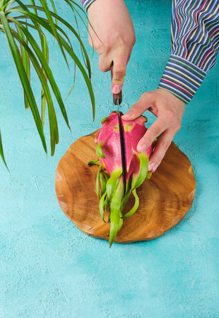 Cutting fresh pink skinned pitahaya or dragon fruit on wooden board on turquoise concrete...