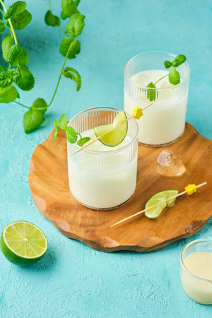 Refreshing drink, Brazilian lemonade made of lime and condensed milk with ice cubes in transparent glasses on wooden gloss on turquoise concrete background. Summer non-alcoholic drinks.の写真素材