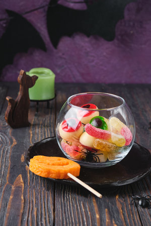 Halloween themed gummy candies in a round glass bowl on a dark wooden background. Halloween celebration, party, themed food and sweets. Happy Halloweenの写真素材