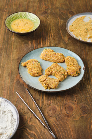 Prepared for deep frying raw chicken nuggets coated with flour, egg and breadcrumbs on ceramic plate...