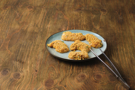 Prepared for deep frying raw chicken nuggets coated with flour, egg and breadcrumbs on ceramic plate on brown wooden background.の写真素材