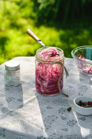 Pickled sliced â€‹â€‹red onion in a clear glass jar with marinade on a table in the yard....