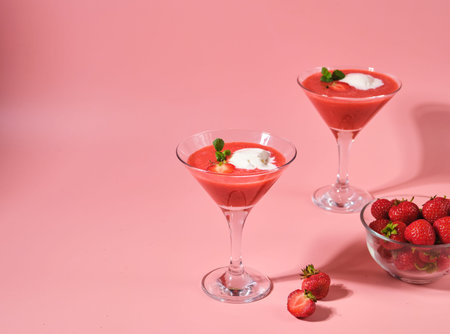 Non-alcoholic strawberry cocktail with ice cream scoop in triangle martini glasses on plain pink background. Valentine's day concept. Summer drinksの写真素材