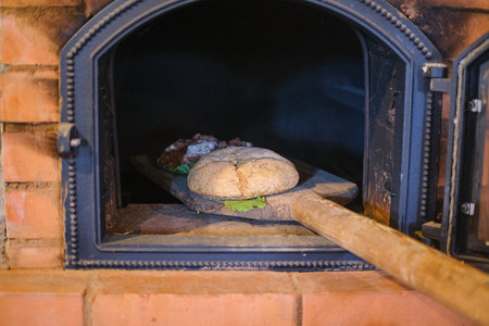 Demonstration of baking bread in a brick oven on a hearth in the ethnographic museum. Ancient crafts, skills. Bread bakingの写真素材