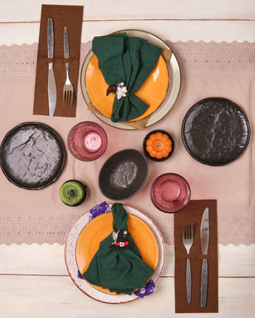 Halloween themed table setting for two with orange plates on wooden background. Halloween party.
