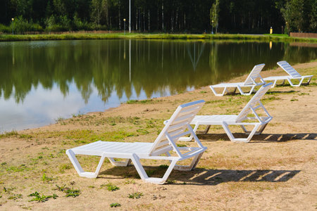 White wooden sun loungers on the shore of a forest lake on the sand. Rest, relaxation. Outdoor recreationの写真素材