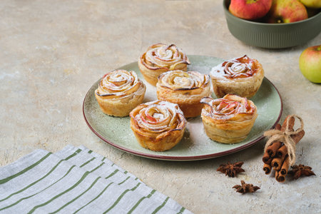 Puff pastry with rose-shaped apples dusted with powdered sugar on a green ceramic plate against a...