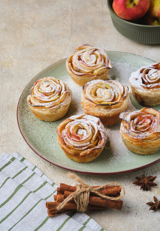 Puff pastry with rose-shaped apples dusted with powdered sugar on a green ceramic plate against a...