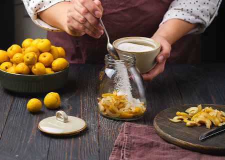 A woman sprinkles sugar over sliced, seeded Japanese quince or Chaenomeles fruits against a wooden background. The fruits are edible shrubs.の写真素材