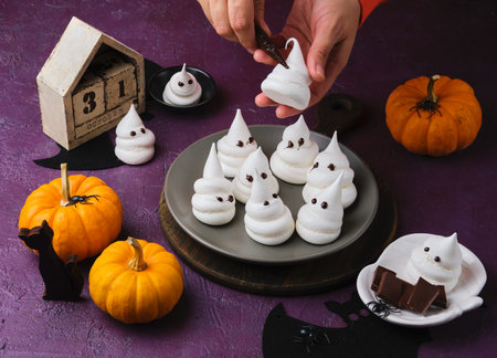 Halloween sweets, meringue ghosts in a gray plate on a purple concrete background. Happy Halloween. Trick or treat. Treats for Halloween parties.の写真素材
