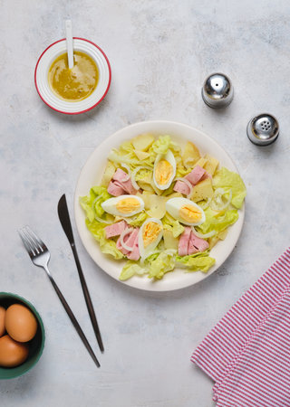 Parisian salad of lettuce, boiled potatoes, ham, and hard-boiled eggs in a light-colored plate against a gray concrete background. Salad as a main course. French cuisineの写真素材