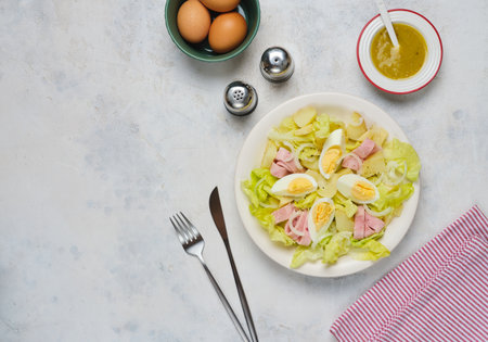 Parisian salad of lettuce, boiled potatoes, ham, and hard-boiled eggs in a light-colored plate against a gray concrete background. Salad as a main course. French cuisineの写真素材