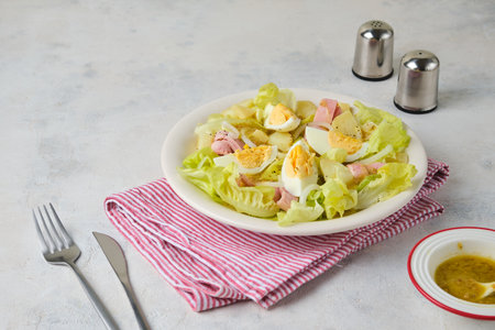 Parisian salad of lettuce, boiled potatoes, ham, and hard-boiled eggs in a light-colored plate against a gray concrete background. Salad as a main course. French cuisineの写真素材