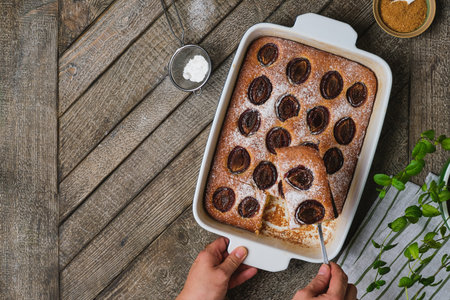 Cornmeal pie with fresh plums dusted with powdered sugar in a rectangular ceramic pan on a wooden background. Seasonal baking. Plum recipes.の写真素材