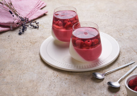 Layered yogurt jelly with raspberry puree and whole raspberries in a layer of clear jelly in clear glass cups against a light concrete background. No-bake dessertsの写真素材