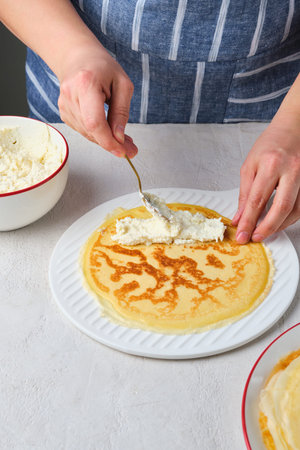Step-by-step instructions for making dessert pancakes with cottage cheese filling on a light concrete background. Step three: wrapping the cottage cheese filling into the pancake. Step-by-step recipesの写真素材