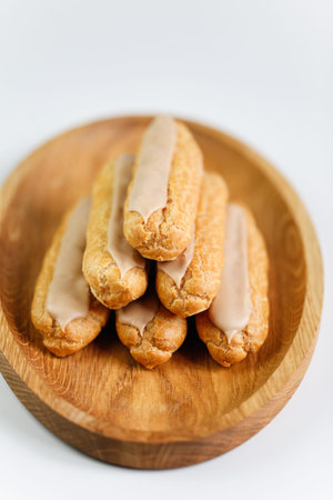 Eclairs on white background with a wooden plate