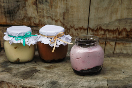 Creamy dessert in a small glass jars with decoration and ribbon on a wooden backgroundの写真素材