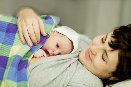happy woman after the birth of a newborn baby on a functional bedの写真素材
