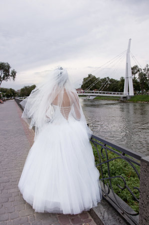 bride stands on the waterfront on background the bridge. の写真素材