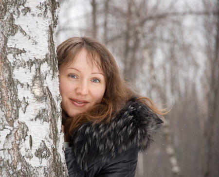 Portrait of beautiful brunette woman near a birch in snow winter park の写真素材
