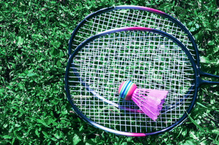 A pink shuttlecock and a badminton racket lie on the green lawn grass at the player's feet in blue sports shoes.の写真素材