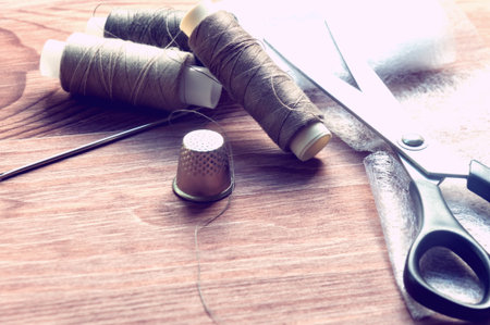 The tailor's desk. Old sewing wooden drums or skeins on an old wooden worktable with scissors. Toning for antiquity.の写真素材