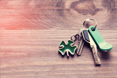 Set of metal and magnetic keys with a keyring-shaped clover leaf in green on a dark wooden backgroundの写真素材