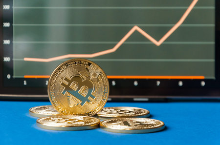Few gold coins of bitcoins lie on the table in front of and next to the tablet on which charts of Bitcoin's cost growth are visible. One silver bitcoin stands side by side on the edge. The concept of crypto currency.の写真素材