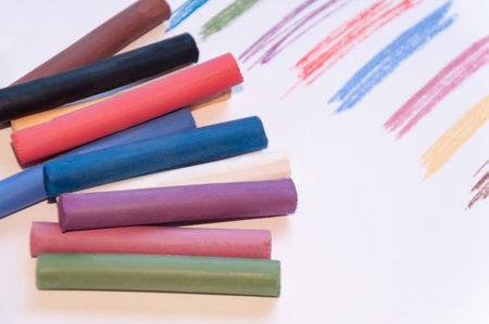 A set of multicolored pastel pencils on a light background with a trail drawn next to it. Selective...