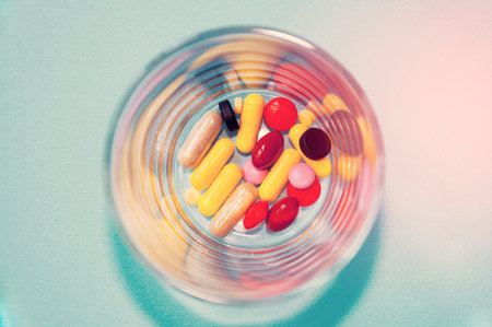 Many different colorful capsules and dragees with medicines in a small transparent glass. The concept of medicineの写真素材