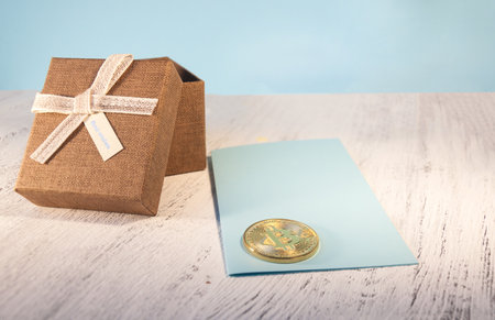 A brown gift box and a beige ribbon with a label on a light background. A Christmas gift. Coin bitcoin. Thinning and blurring.の写真素材