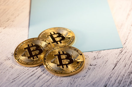 Several coins of crypto currency Bitcoin lies on a blue postcard on a white wooden background....