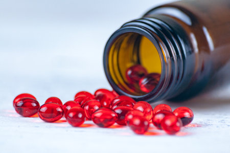 Red capsules with medicine or vitamins in liquid form lie on a white background. Capsules are scattered from a small jarの写真素材