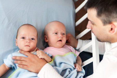 Young father with his newborn twins lying in bed. Selective focus.の写真素材