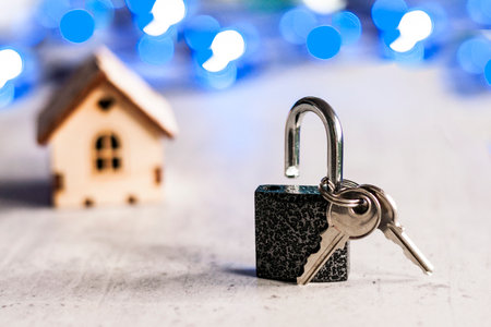 Model of a wooden house with a lock and keys and bokeh on a gray background. Mortgage concept. Selective focus.の写真素材
