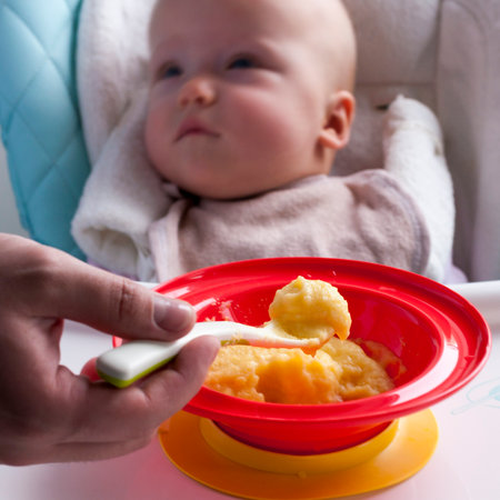 Young dad feeds the child porridge from a bright red plate. Selective focusの写真素材