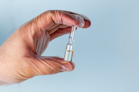 Male hand in a transparent medical nitrile glove holds a vial of medication. Medicine conceptの写真素材