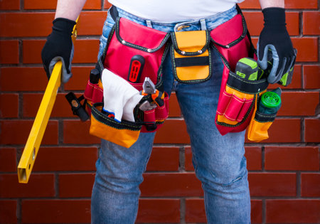Man with standing level in his hand against the background of a red brick wall with a full tool bag....